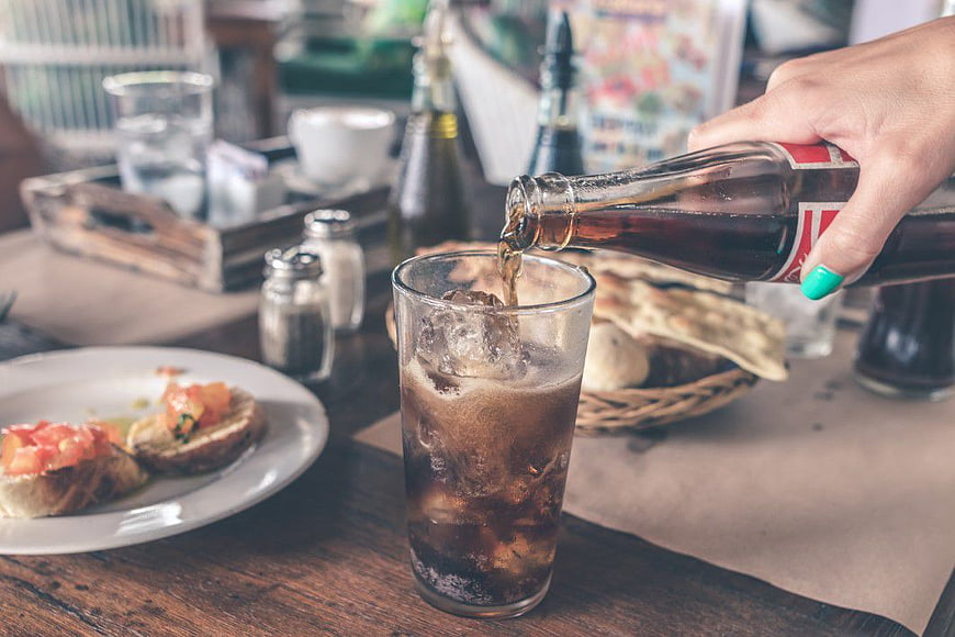 Pouring Cola into Glass with Ice at Restaurant Table