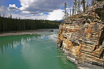 Turquoise river flowing past layered rock cliffs and pine forest