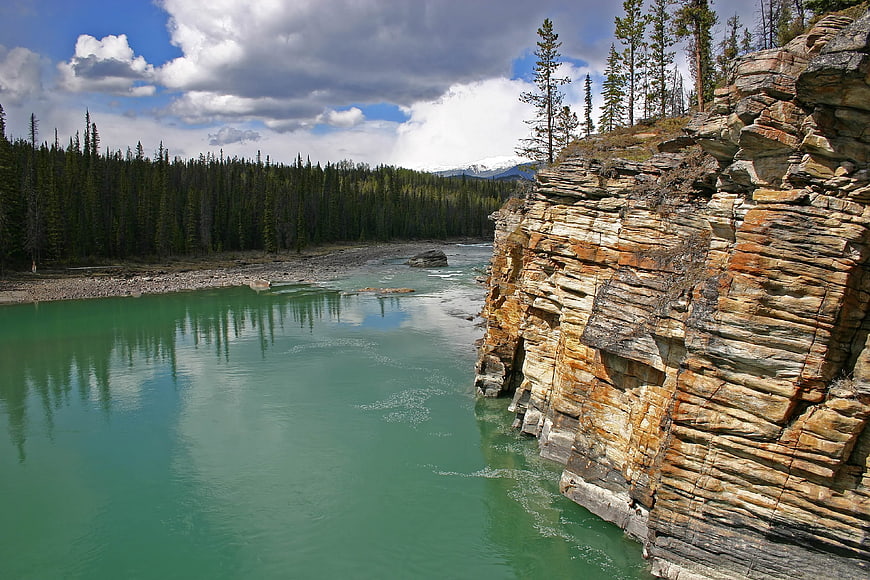 Turquoise river flowing past layered rock cliffs and pine forest