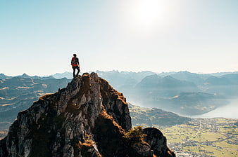 Man standing on rocky mountain peak overlooking vast valley and distant peaks