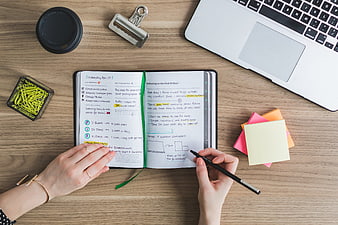 Top view of hands writing in planner on wooden desk