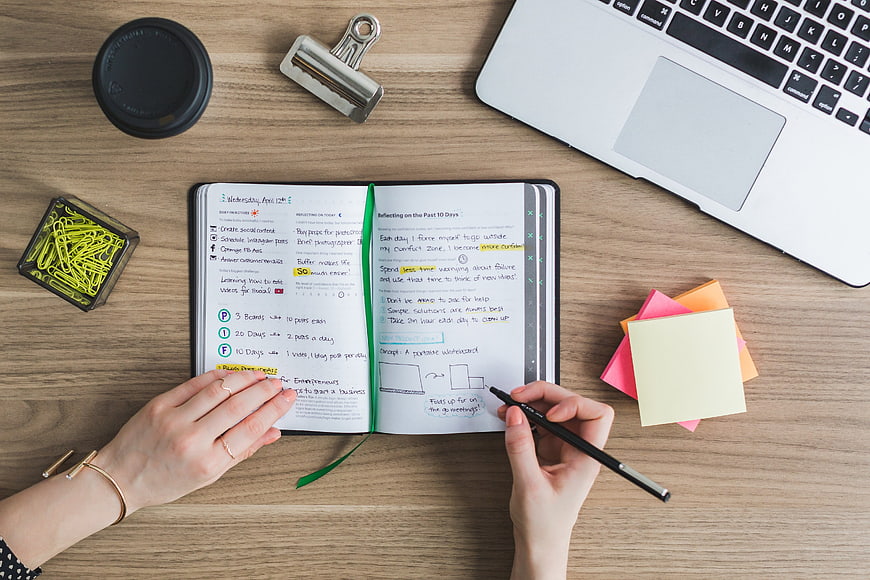 Top view of hands writing in planner on wooden desk