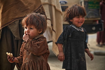 Two young children in dusty clothes eating outdoors