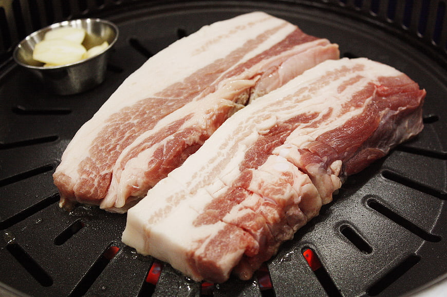Raw pork belly slices on a Korean BBQ grill