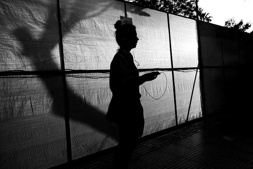 Silhouette of Woman Walking with Earphones Against Wall