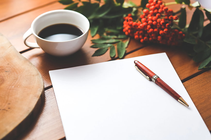 Blank paper, pen, and coffee cup on wooden table