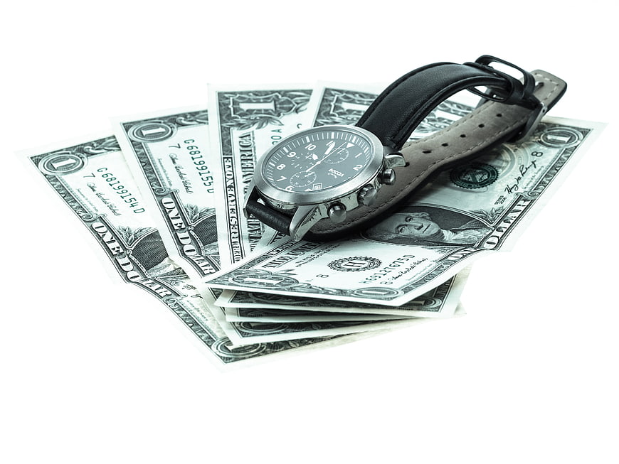 Silver Chronograph Watch Resting On Fanned US Dollar Bills