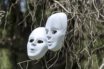 Two white anonymous masks hanging on bare tree branches in nature
