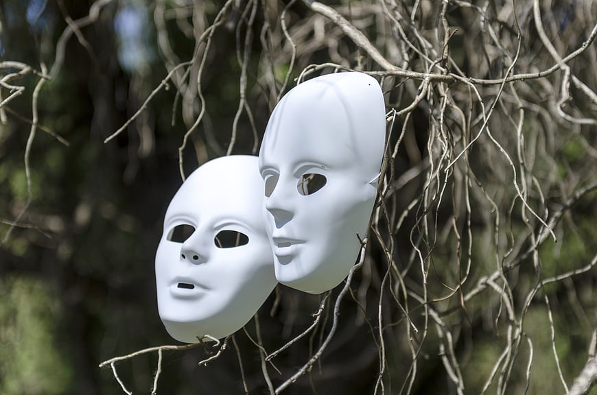Two white anonymous masks hanging on bare tree branches in nature
