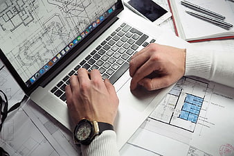 Architect working on laptop with blueprints and watch