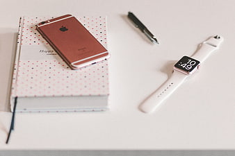 Flat lay of rose gold iPhone, smartwatch, and polka dot notebook