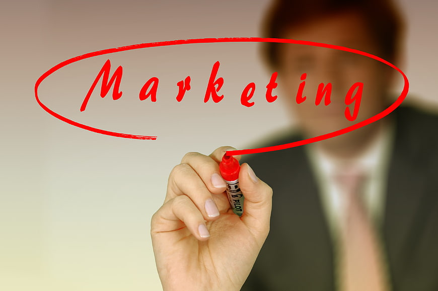 Businessman writing Marketing on transparent board with red marker