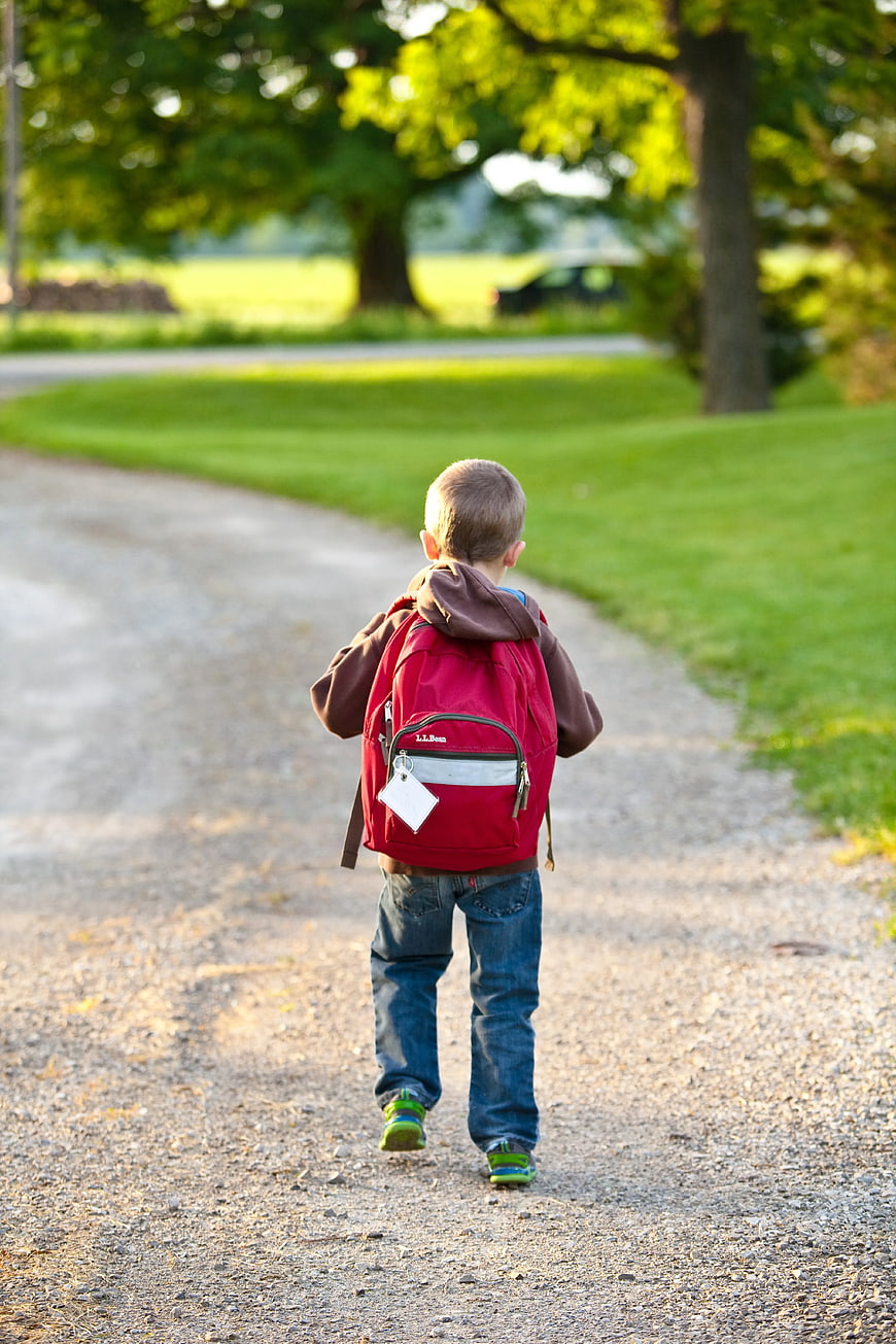 Young Boy Walking Away on Gravel Path with Red Backpack