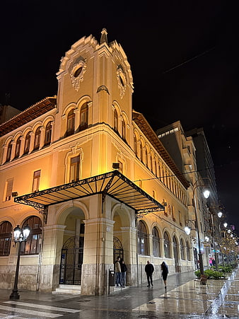 Illuminated historic building facade at night with wet street reflections