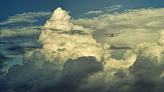 Biplane flying past dramatic cumulus clouds in a moody sky