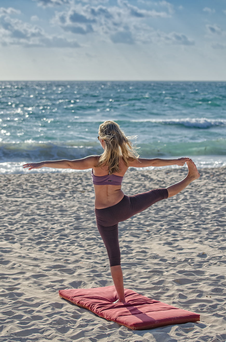 Woman doing yoga on a beach mat facing the ocean