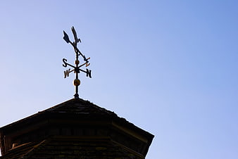 Silhouette of weather vane on roof against blue sky