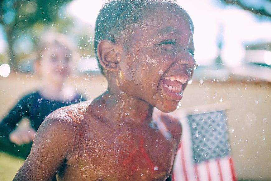 Laughing African American Boy Playing in Water Sprinkler