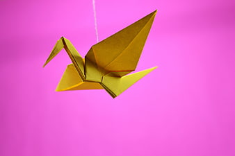 Yellow Origami Crane Hanging Against Vibrant Pink Background