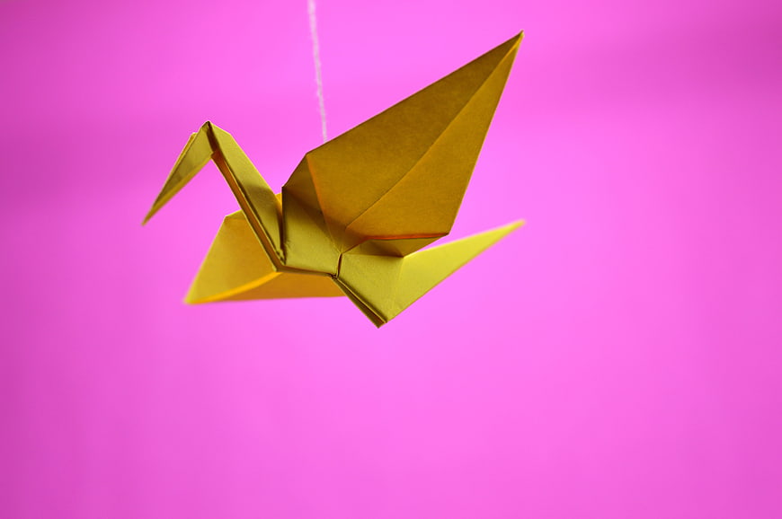 Yellow Origami Crane Hanging Against Vibrant Pink Background