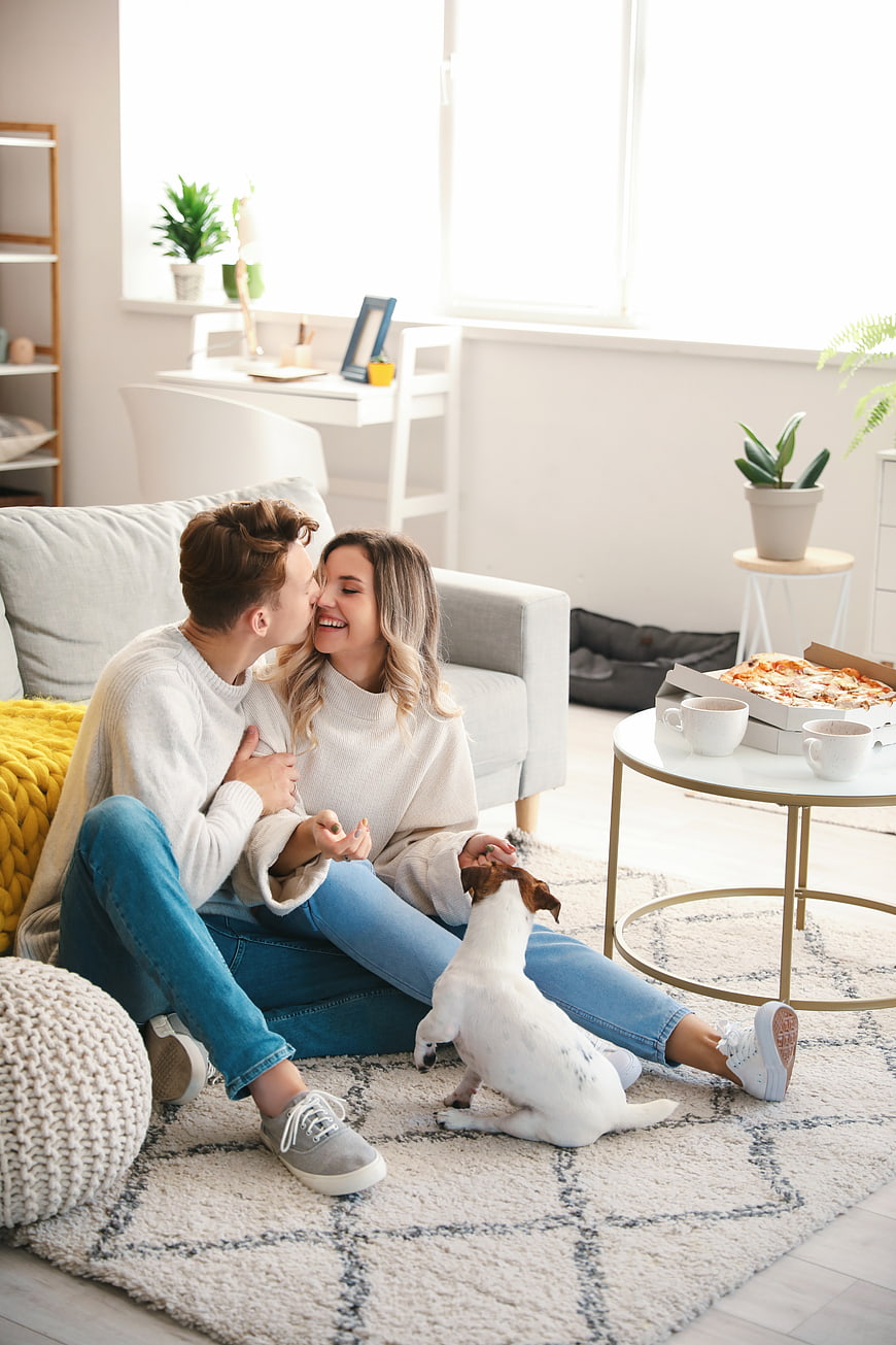 Happy couple kissing on living room floor with dog and pizza