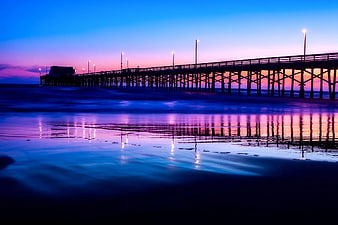 Silhouette of wooden pier at twilight with vibrant purple and blue reflections