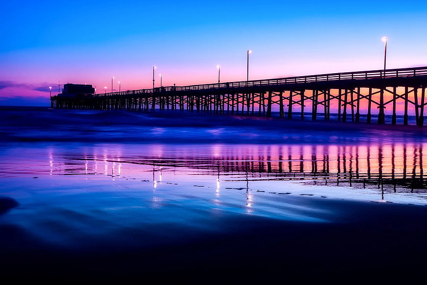 Silhouette of wooden pier at twilight with vibrant purple and blue reflections