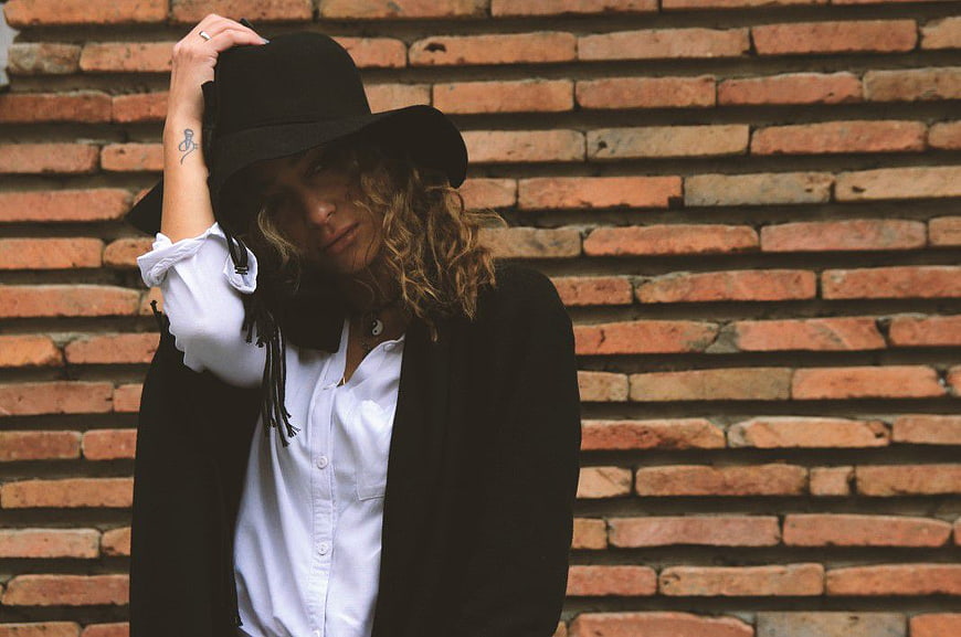Stylish woman in black hat posing against brick wall