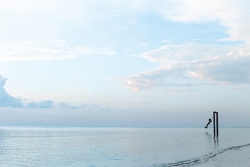 Person swinging on a swing over calm ocean water