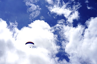 Paraglider soaring through blue sky with white clouds
