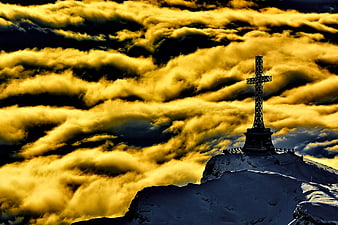 Dramatic Cross on Snowy Mountain Peak Above Golden Clouds