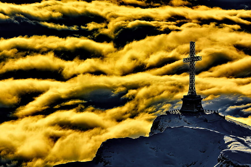 Dramatic Cross on Snowy Mountain Peak Above Golden Clouds