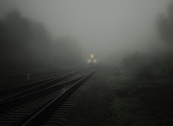 Train emerging from thick fog on railway tracks at night