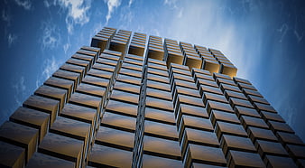 Low angle view of modern geometric skyscraper facade against blue sky
