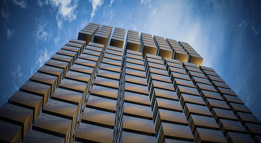Low angle view of modern geometric skyscraper facade against blue sky