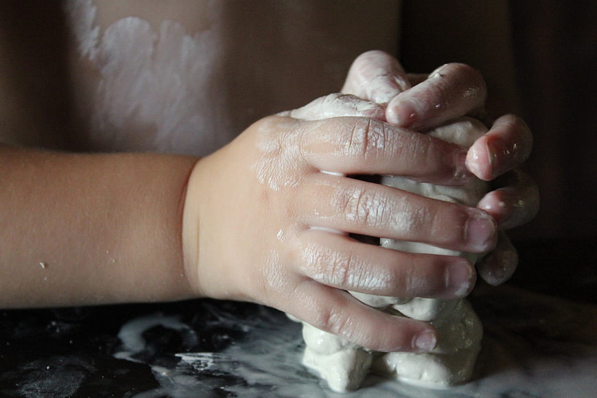 Child's hands kneading dough on dark surface
