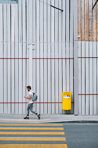 Man walking past yellow mailbox on urban street