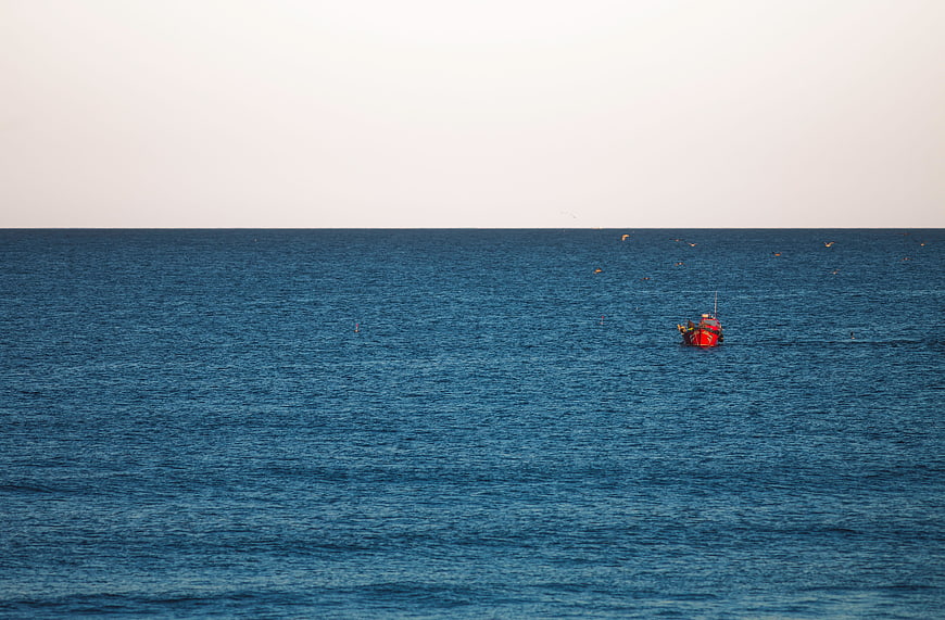 Lone Red Fishing Boat on Calm Blue Ocean Horizon