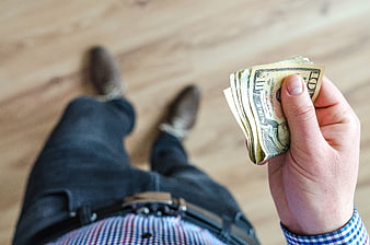 First-person view of hand holding cash on wooden floor