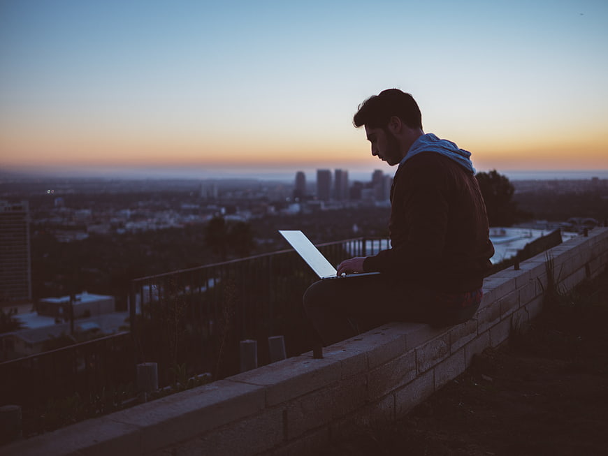 Man working on laptop overlooking city skyline at sunset