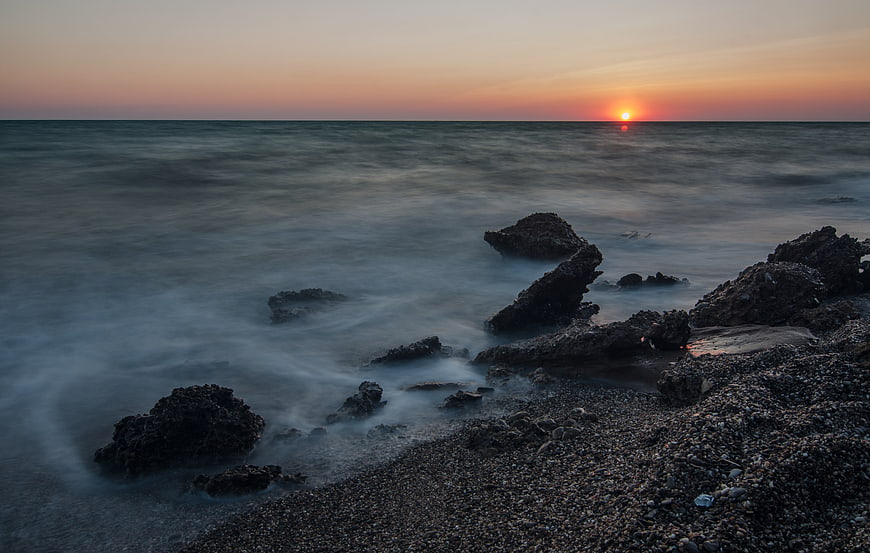 Long Exposure Sunset Over Rocky Pebble Beach with Misty Ocean Waves
