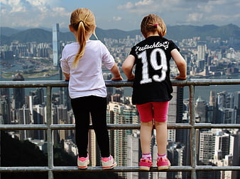 Two young girls standing on a railing overlooking a dense city skyline