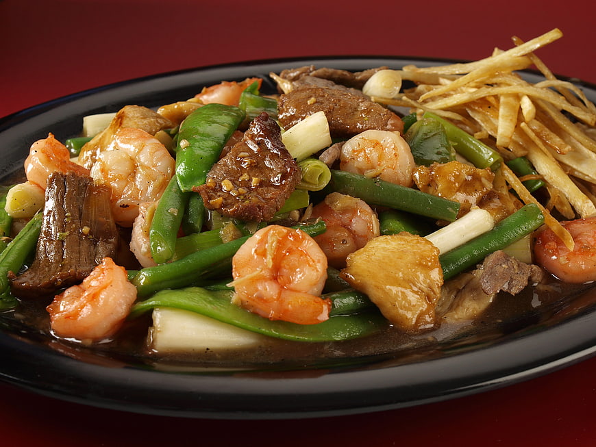 Close-up of stir-fried shrimp, beef, and vegetables on a black plate