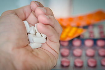 Hand holding white pills with blurred medicine blister packs background