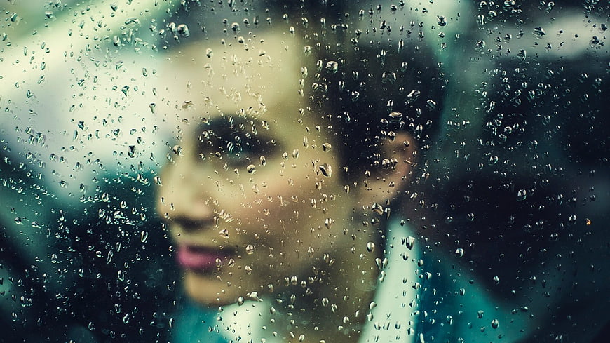 Woman looking out rainy window with water droplets