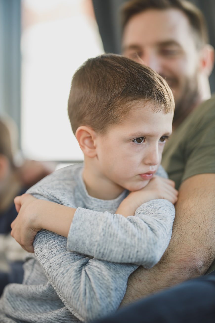 Sad young boy resting head on father's arm