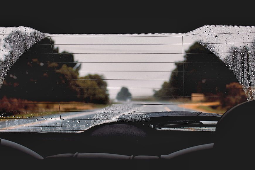 Rainy Road View Through Car Rear Window with Water Drops