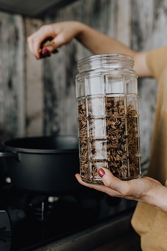Woman holding glass jar of dried pasta in kitchen