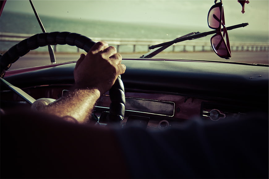 Man driving vintage car with sunglasses on windshield