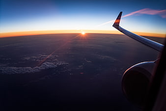 Airplane wing view of sunset over clouds and ocean